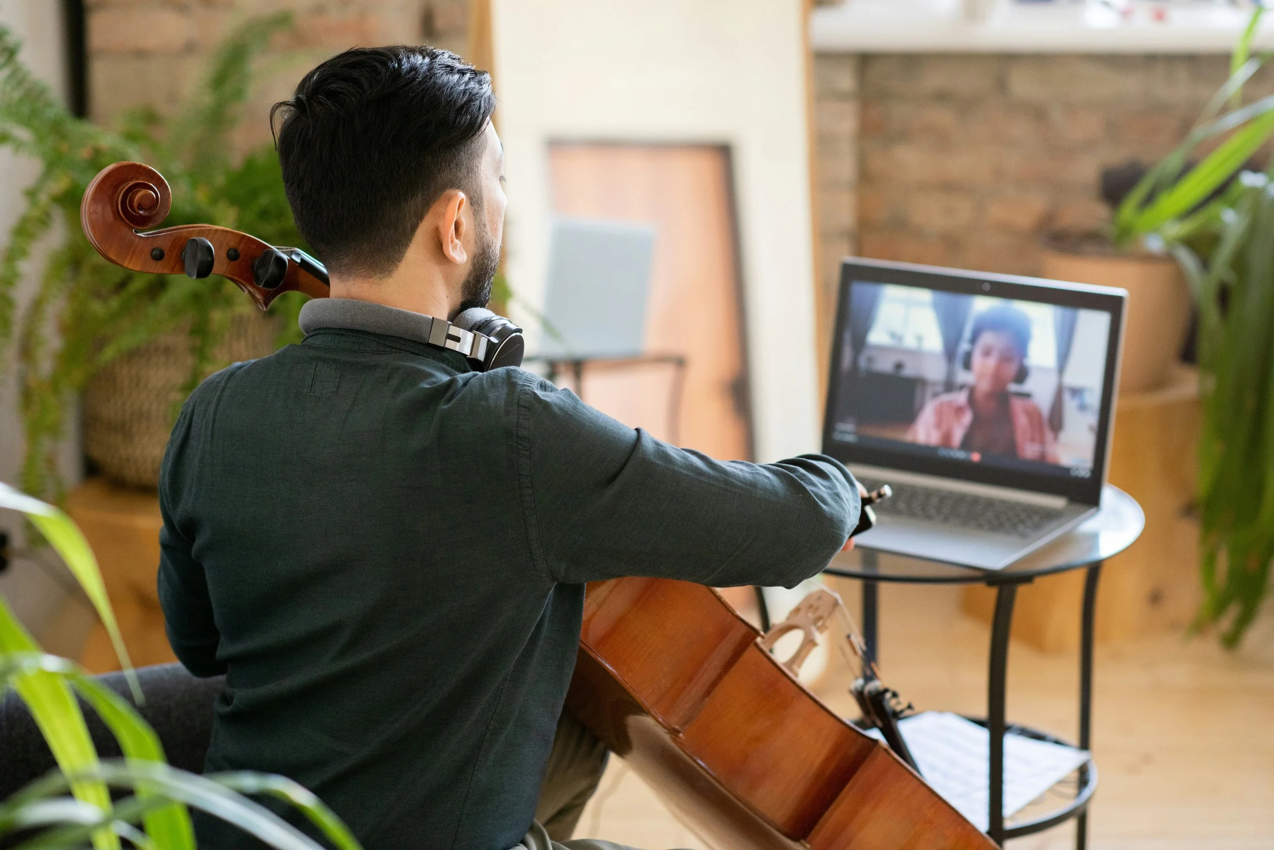 Man with a cello and headphones participating in a virtual meeting on a laptop.