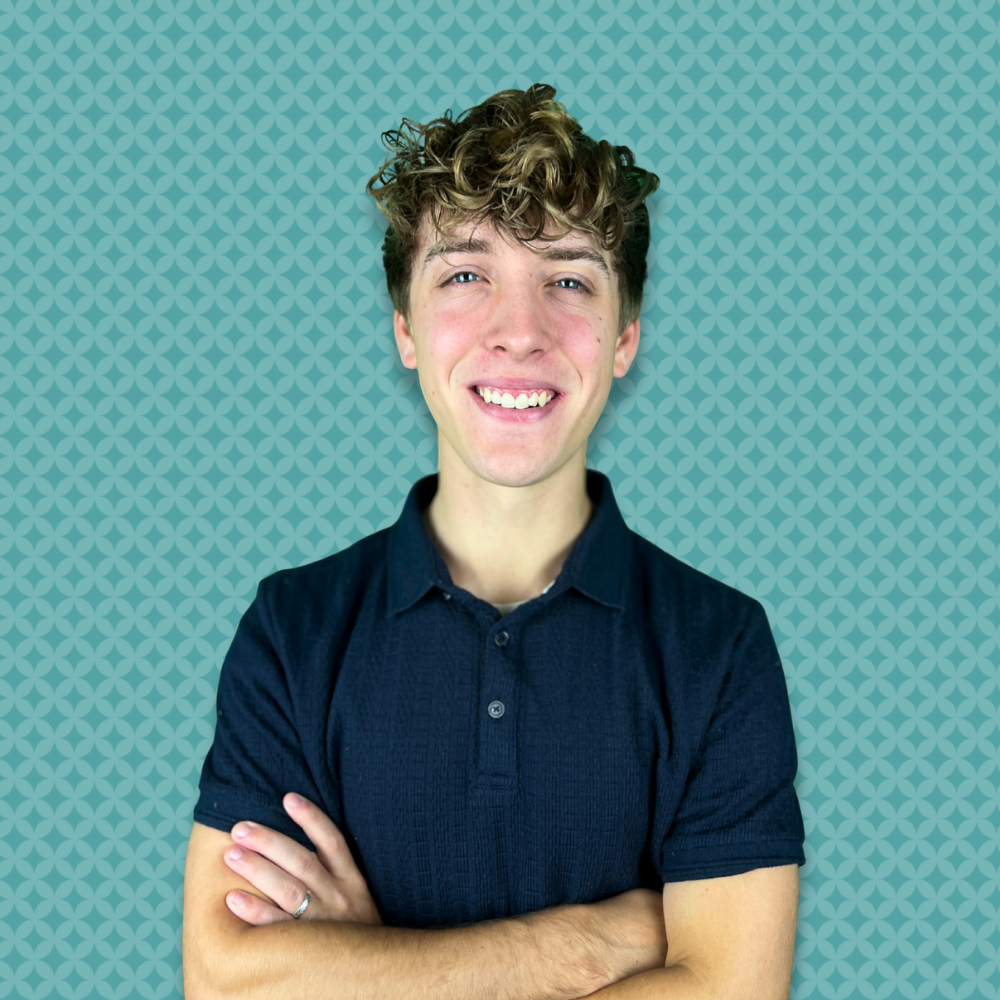A young man with curly light brown hair smiling with arms crossed, standing against a teal patterned background.