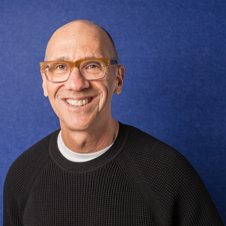 Portrait of a smiling man with glasses against a blue background.