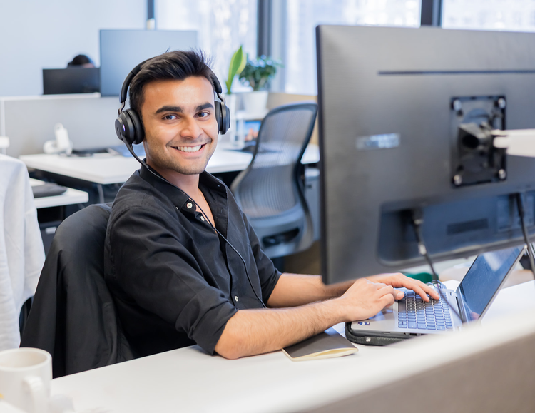 Smiling man wearing headphones working at a computer in an office