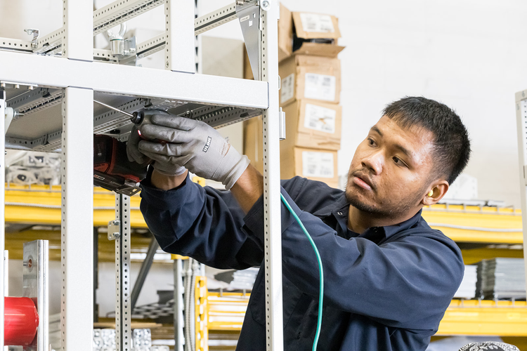 A man wearing gloves and ear protection working on electrical equipment in a warehouse or store room.