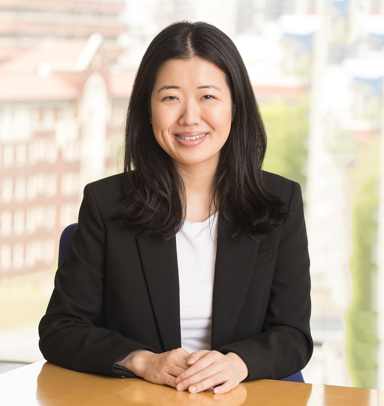 Professional woman smiling while sitting at a table with a city view in the background.