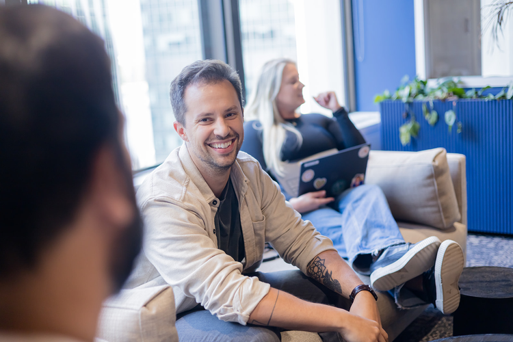 People sitting on a sofa in a modern office lounge, chatting and smiling.