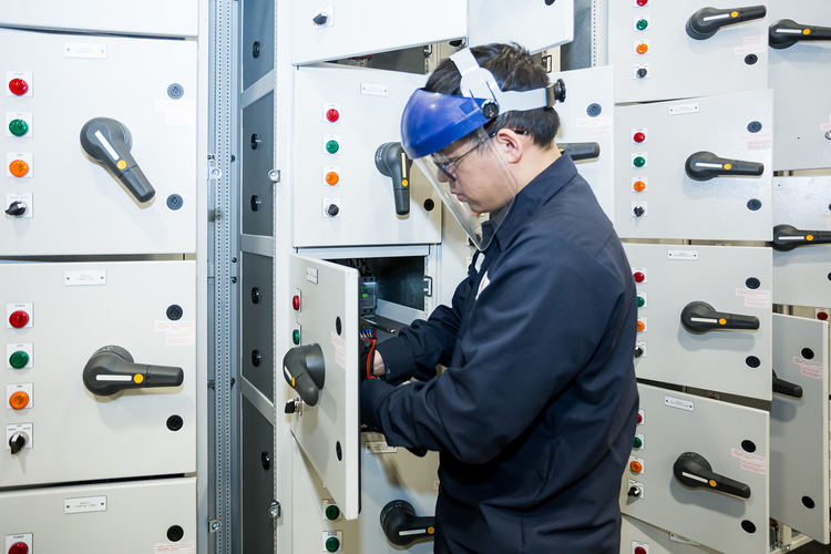 Electrician working on electrical control panel with switches and circuits in an industrial setting