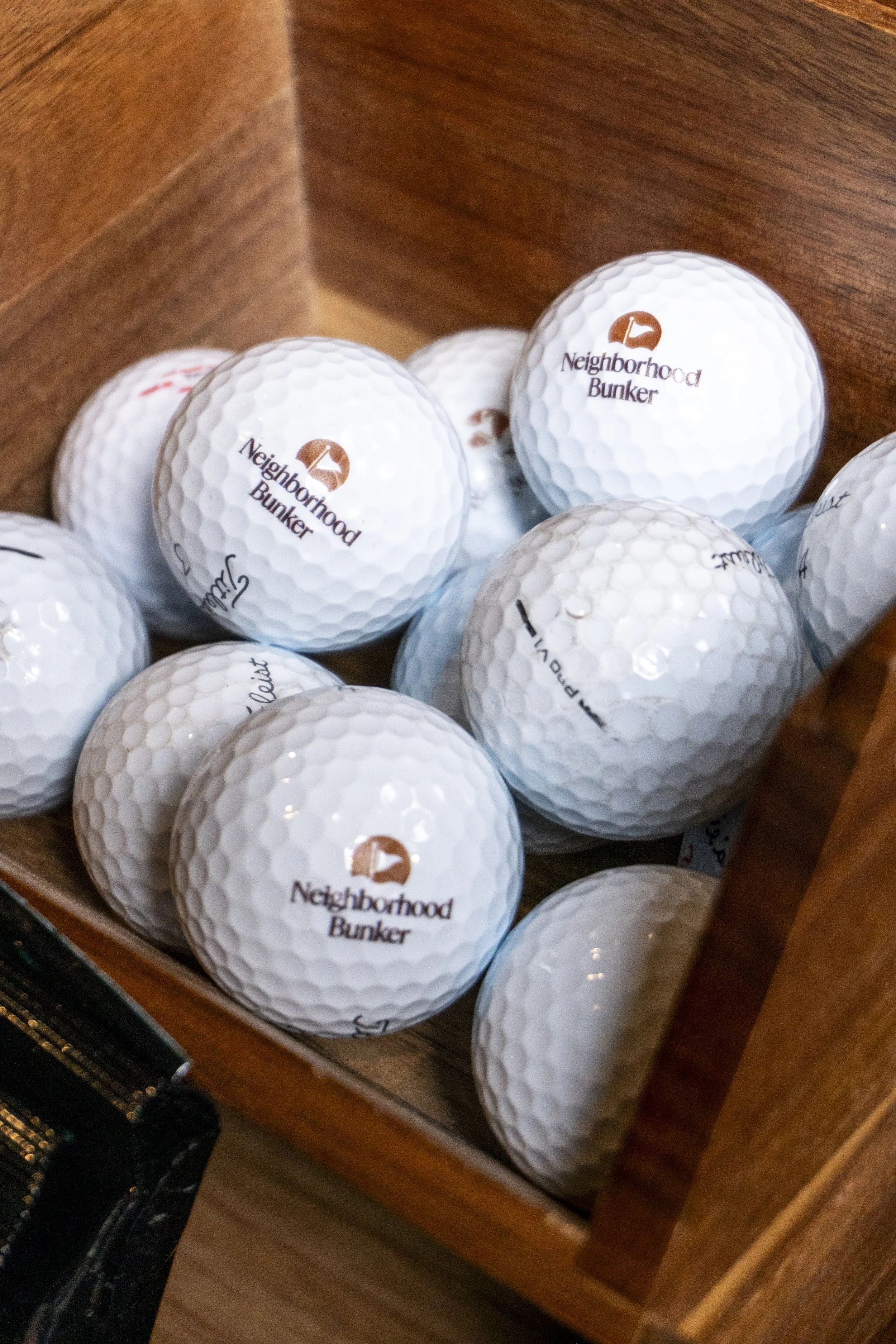 A wooden drawer containing several white golf balls with the logo 'Neighborhood Bunker' printed on them.