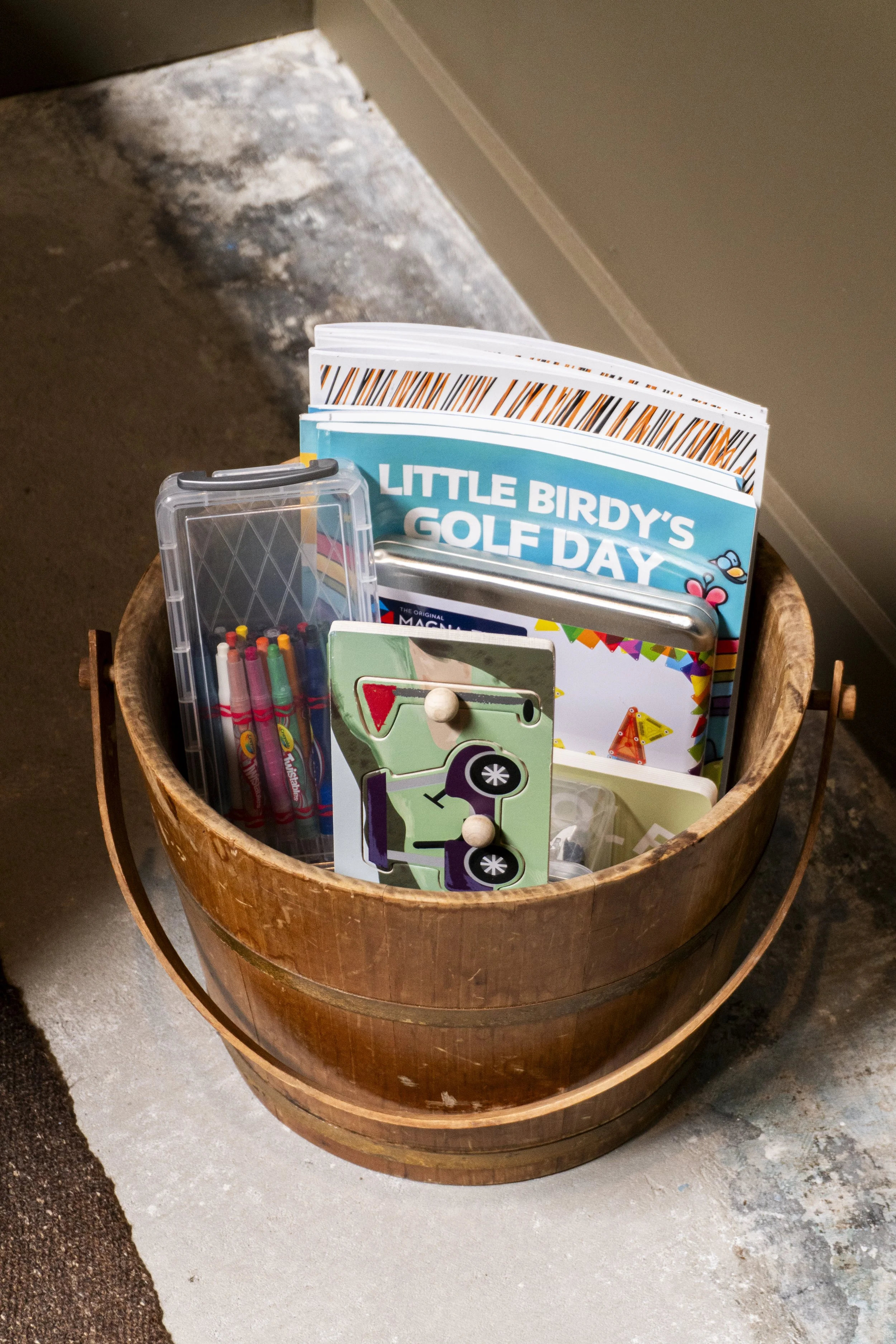 Wooden bucket filled with school supplies including notebooks, pens, markers, and a box labeled 'Little Birdy's Golf Day'.