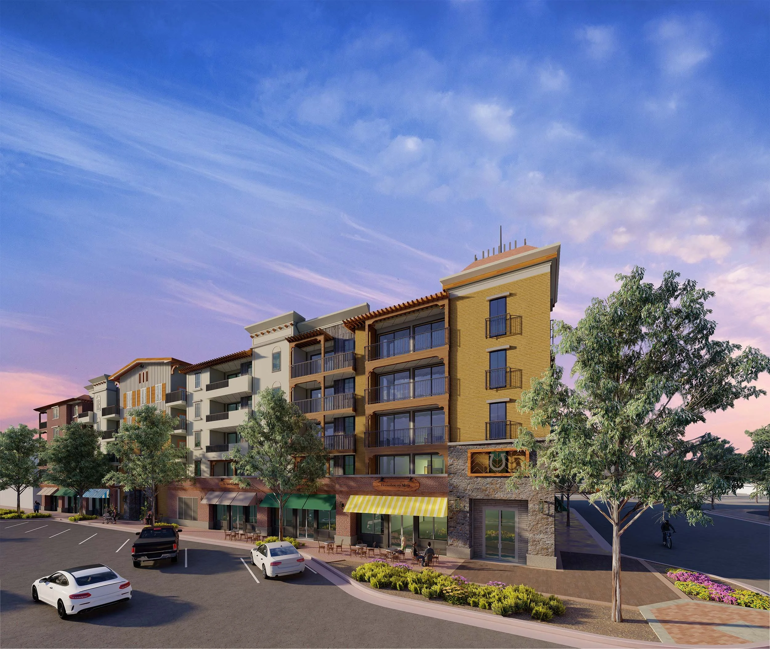 A modern multi-story residential building with shops on the ground floor, featuring balconies, large windows, and trees in a parking lot at sunset.
