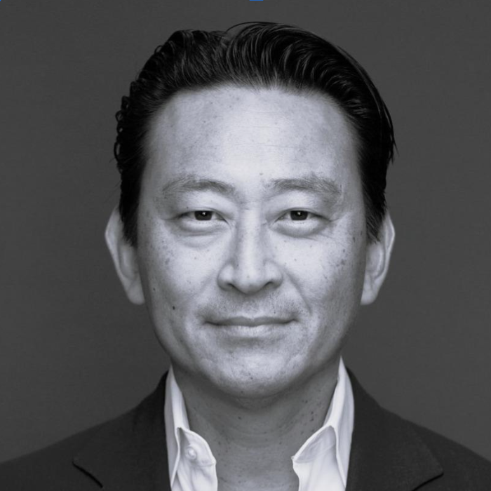 Black and white portrait of a man with slicked-back hair wearing a suit and white shirt, smiling slightly.