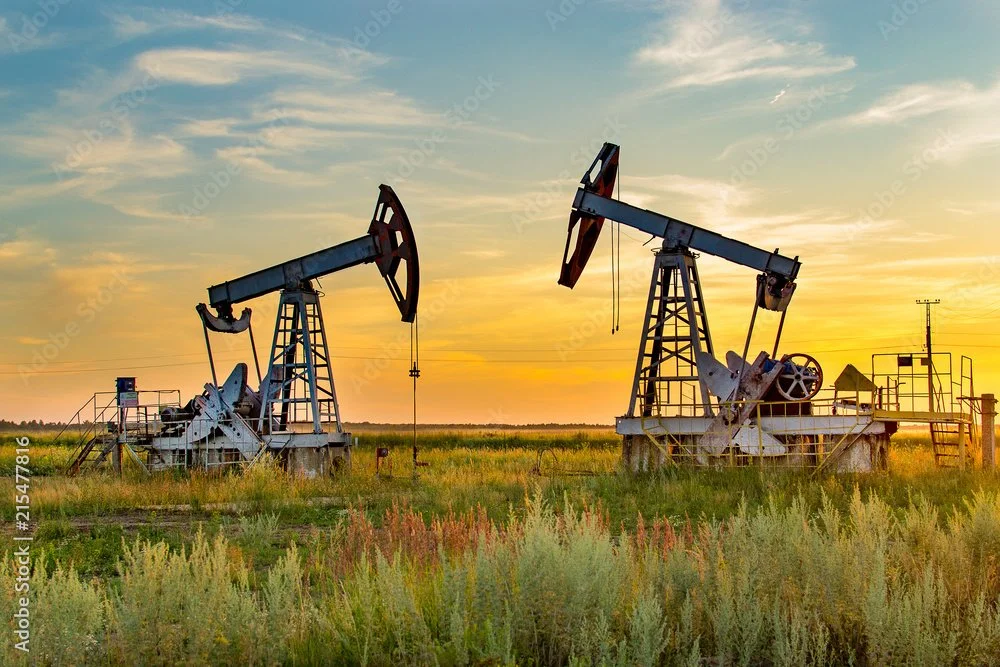 Two oil pumpjacks in a grassy field at sunset.