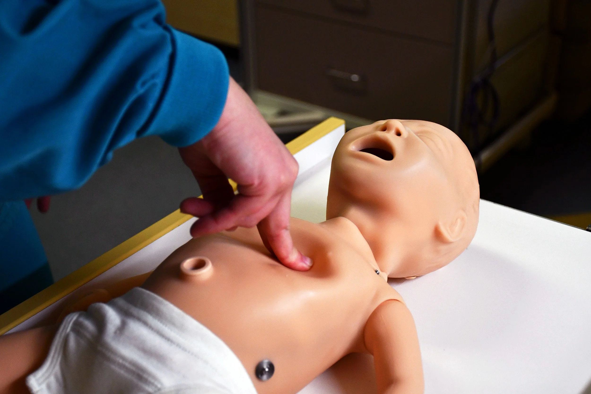 A person performing a medical or CPR training on a baby mannequin.