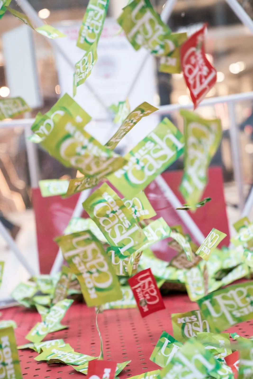 A red vending machine releasing numerous green and red tickets or coupons into the air, with some tickets still inside the machine and others falling onto a red surface below.