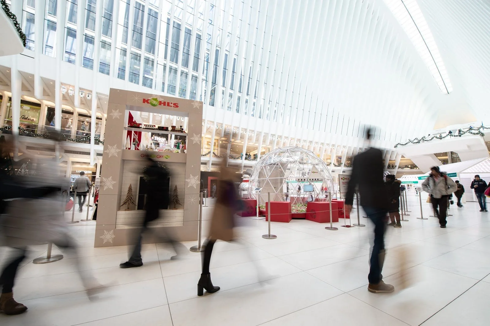 People walking inside a modern shopping mall with Christmas decorations and a Kiehl's holiday display.