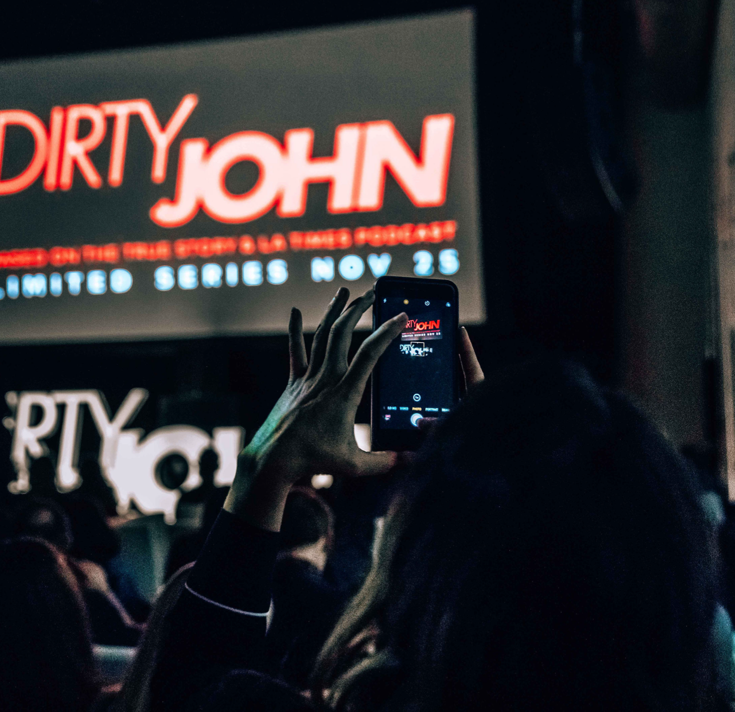 Person taking a photo of a promotional poster for the show 'Dirty John' on their smartphone during a screening or event.