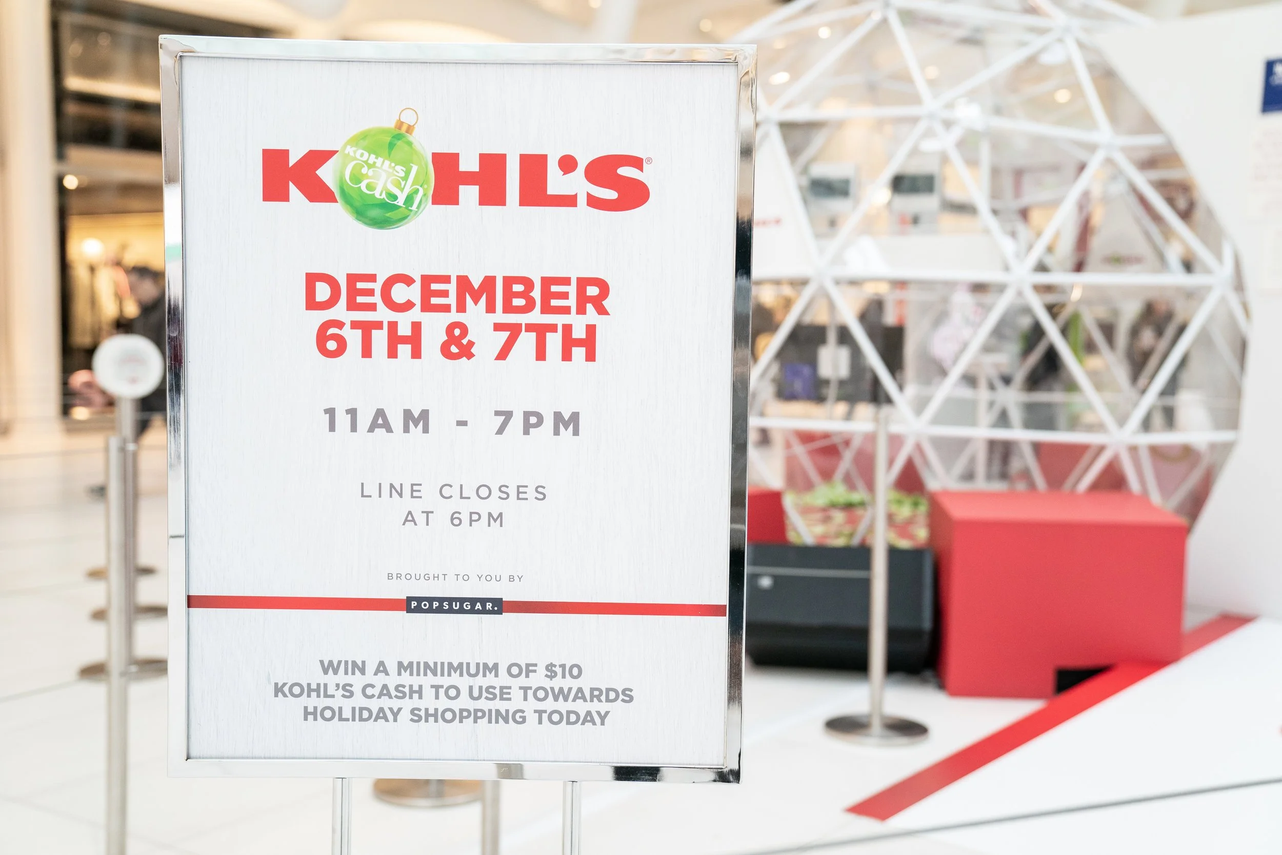 Kohl's store sign announcing holiday shopping event on December 6th and 7th from 11 am to 7 pm, with line closure at 6 pm, and a promotion to win Kohl's Cash for holiday shopping.