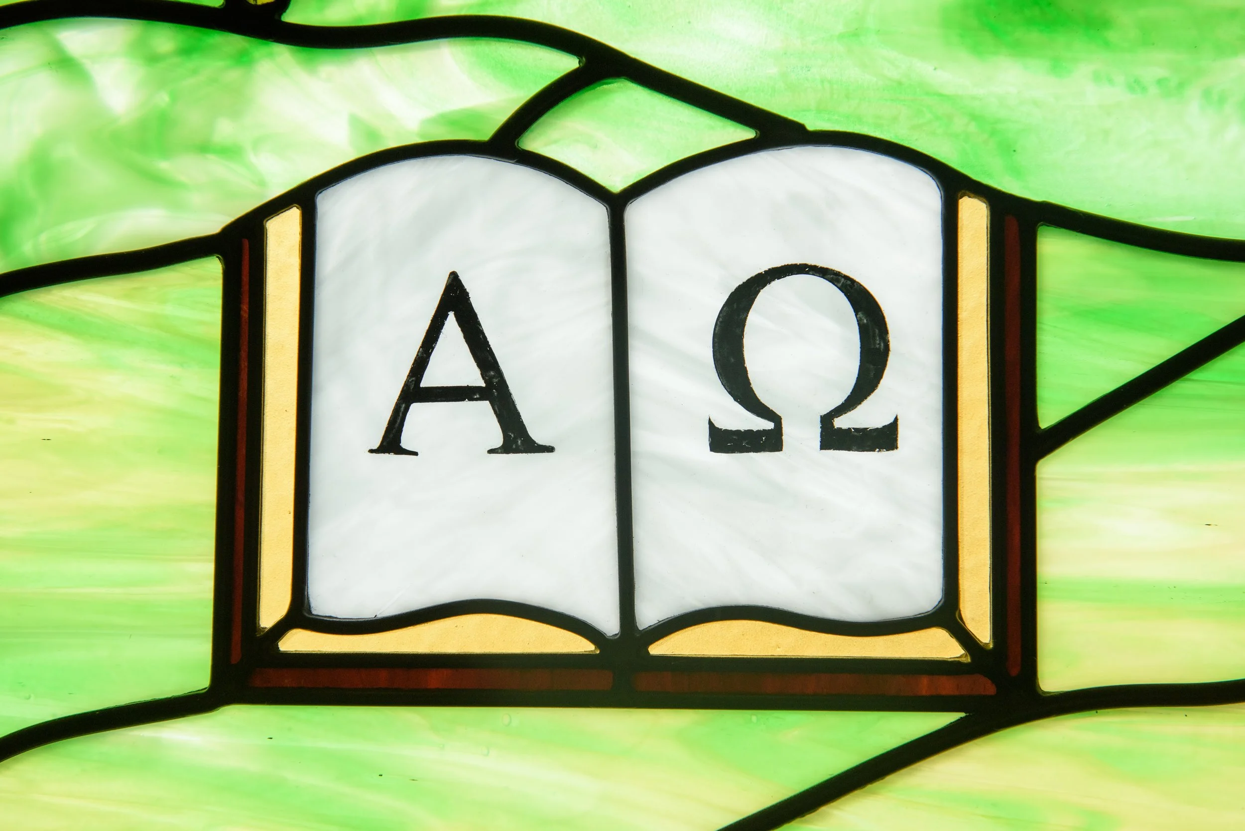 Close-up of a stained-glass window featuring Greek alpha and omega symbols on a bright green background