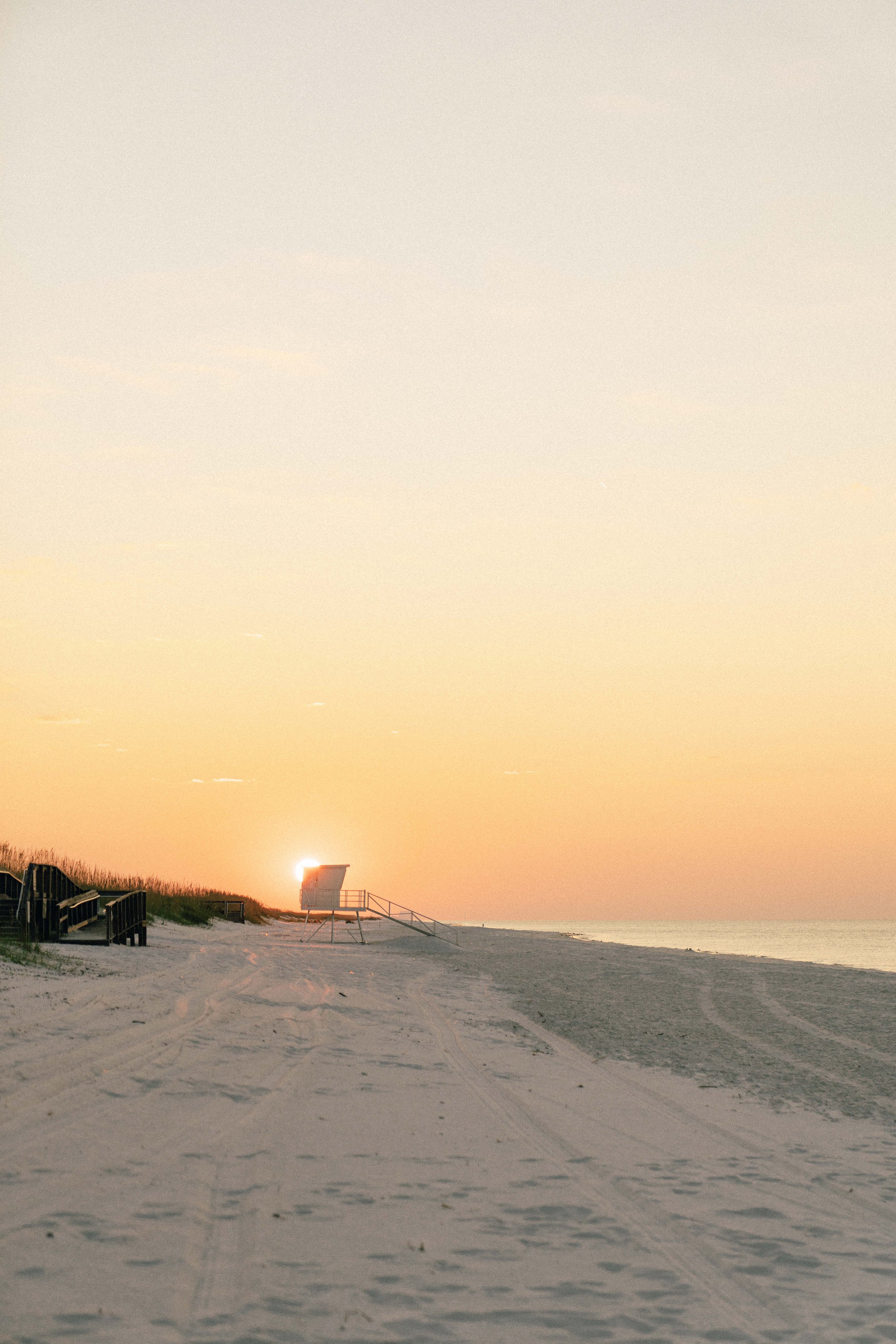 Empty beach at sunrise with a lifeguard stand and footprints in the sand.
