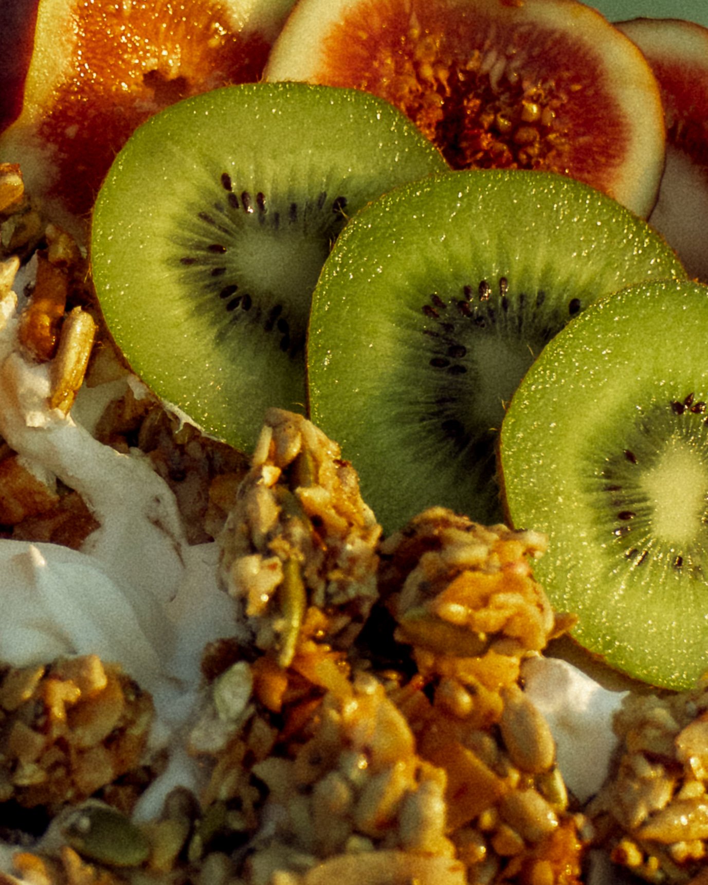 Sliced kiwi and fig on a surface with granola and yogurt.