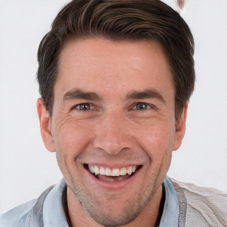 Close-up of a smiling man with short brown hair and blue eyes, wearing a light-colored shirt.