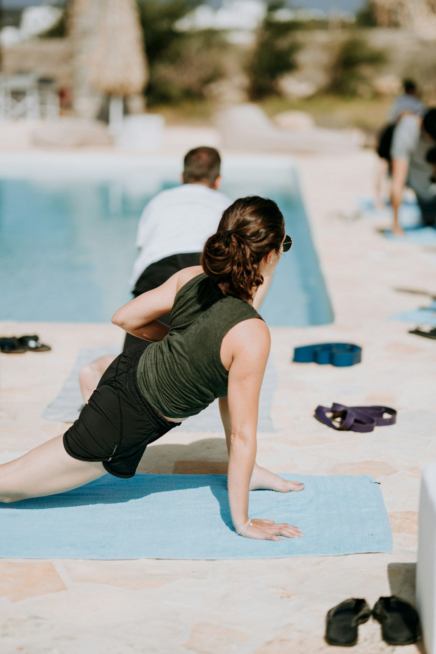 People practicing yoga on mats next to a swimming pool outdoors.