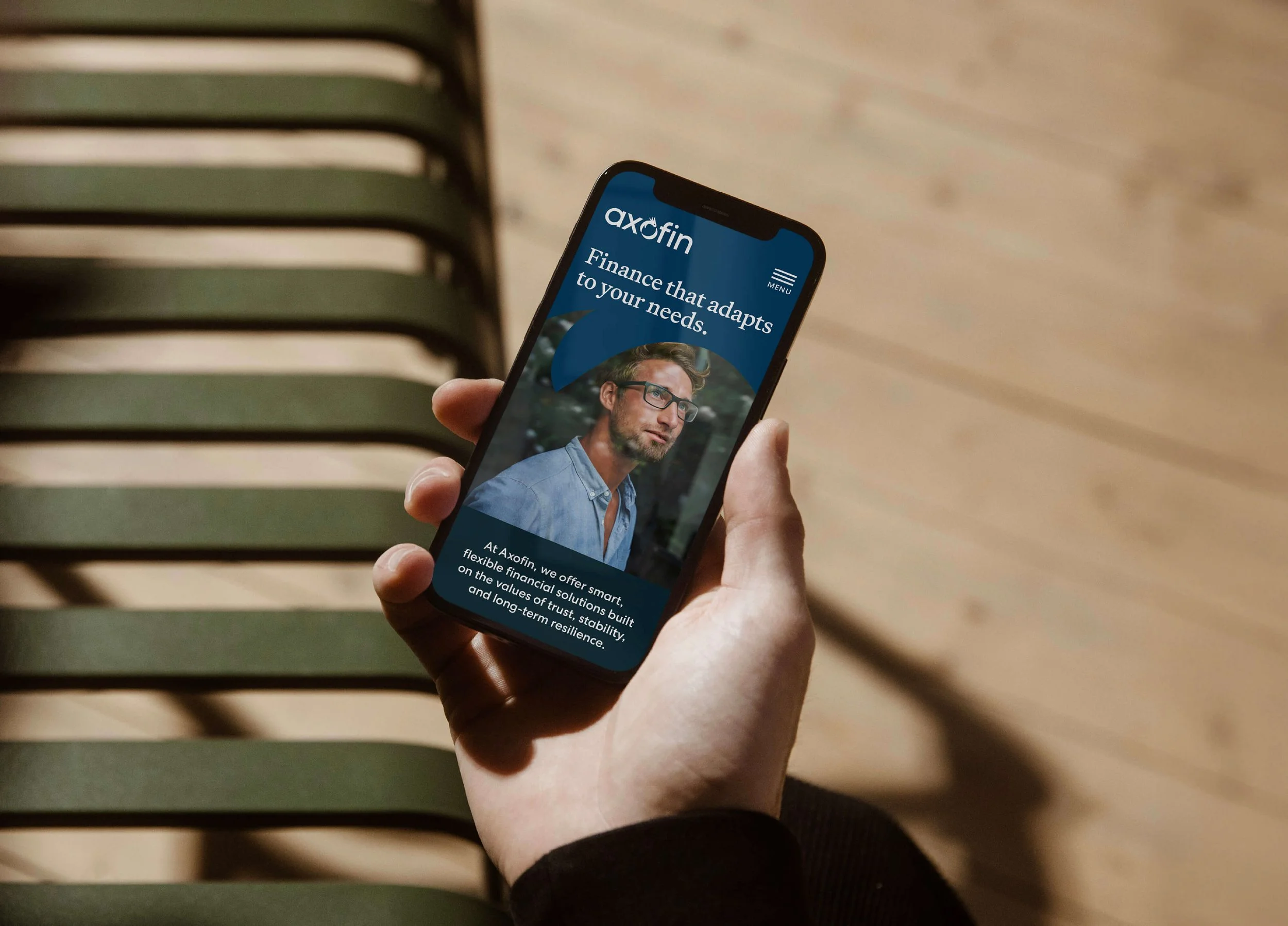 Close-up of a hand holding a smartphone displaying the Axofin website with a man wearing glasses and a blue shirt, and text about financial solutions.