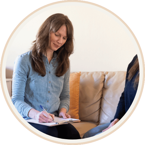 Woman completing health intake paperwork on a clipboard while seated on a couch, representing the new patient onboarding process at Current Wellness
