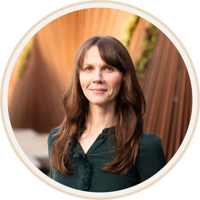 Jennifer Peterson of Current Wellness with long brown hair and blue eyes wearing a dark green blouse, standing outdoors with a wooden fence and greenery in the background.