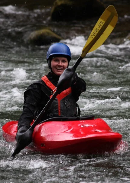Person kayaking in a river with a blue helmet and yellow paddle.