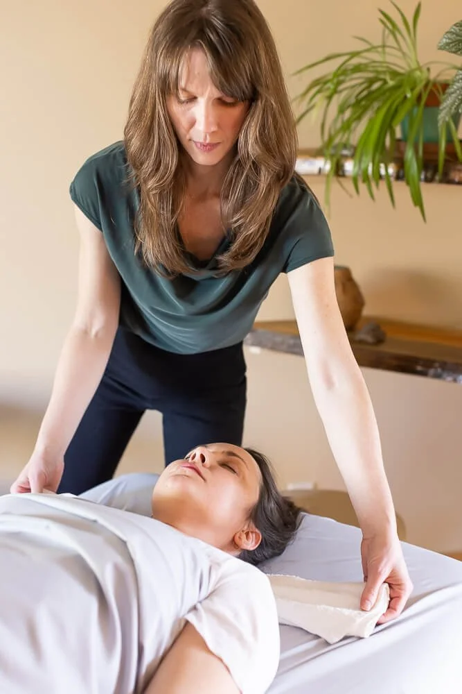 A woman with brown hair giving chest compressions to a woman lying on a bed, indicating a medical emergency or CPR.