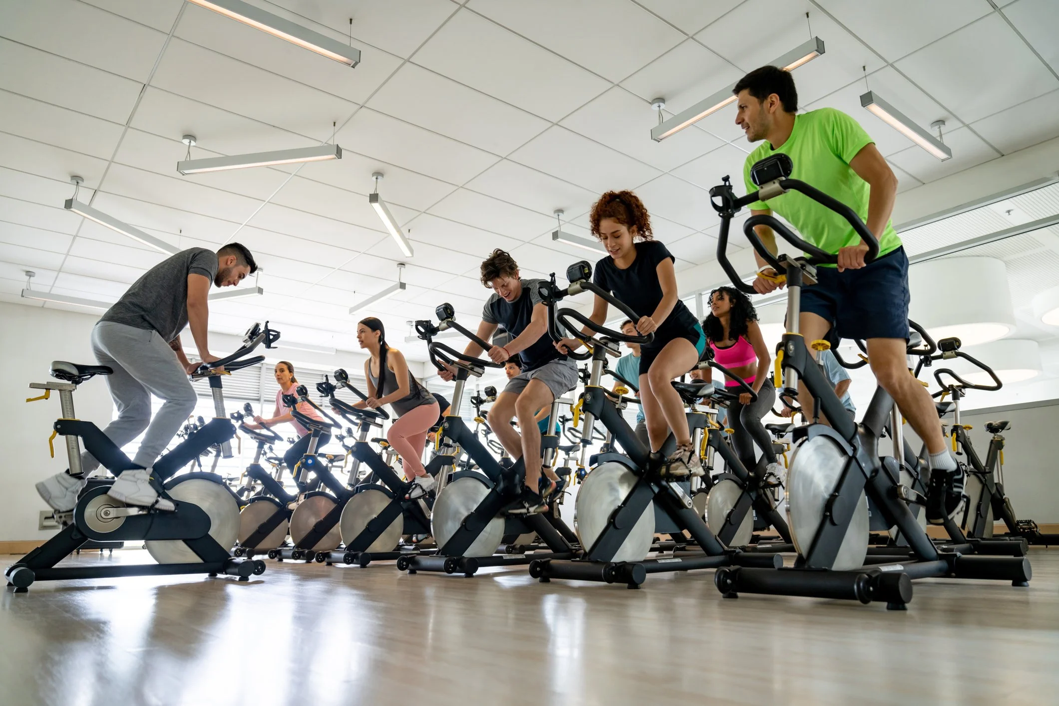 People participating in a group indoor cycling class, riding stationary bikes in a fitness studio