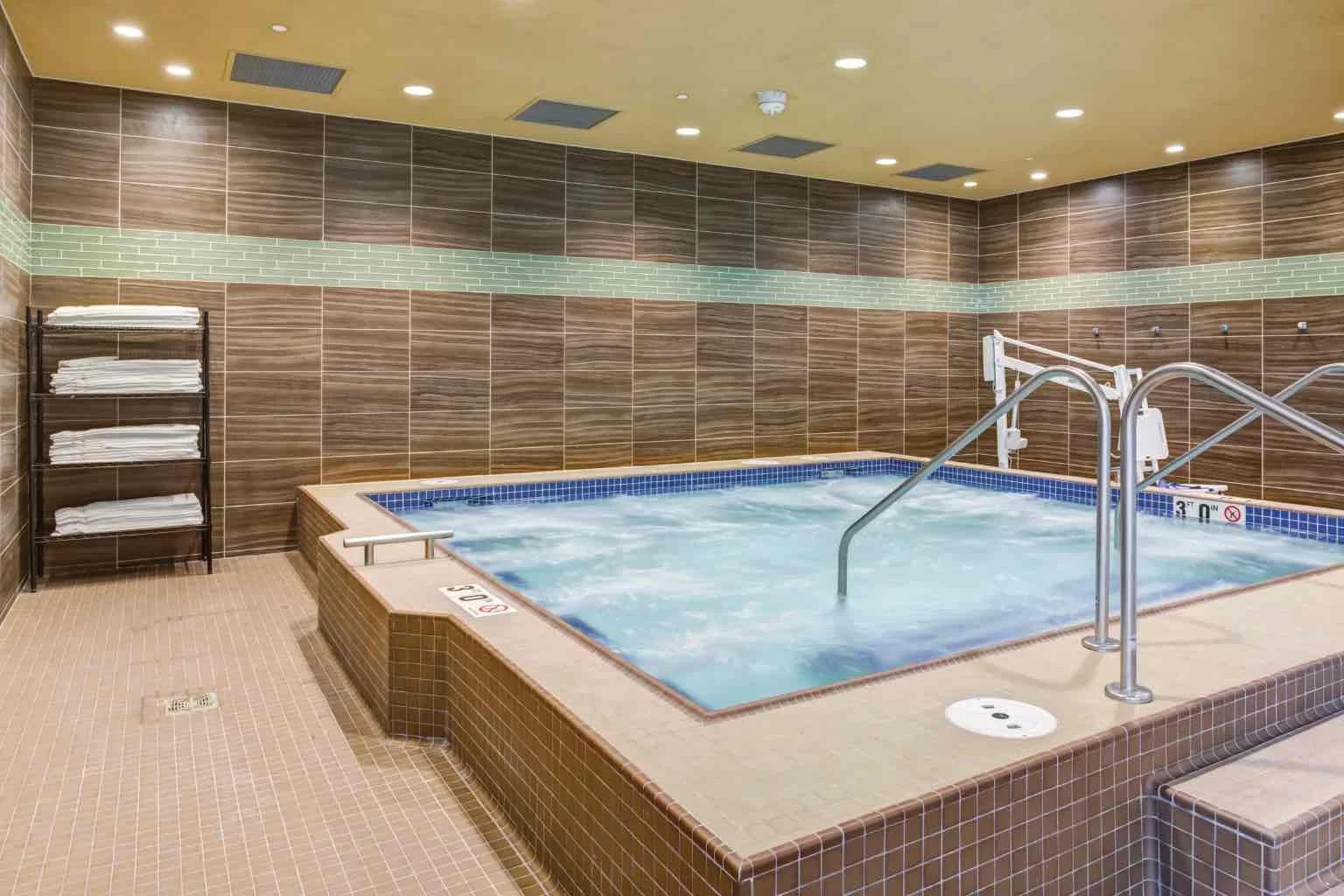 Indoor hot tub with brown and beige tiled walls and floor, with towels on a rack
