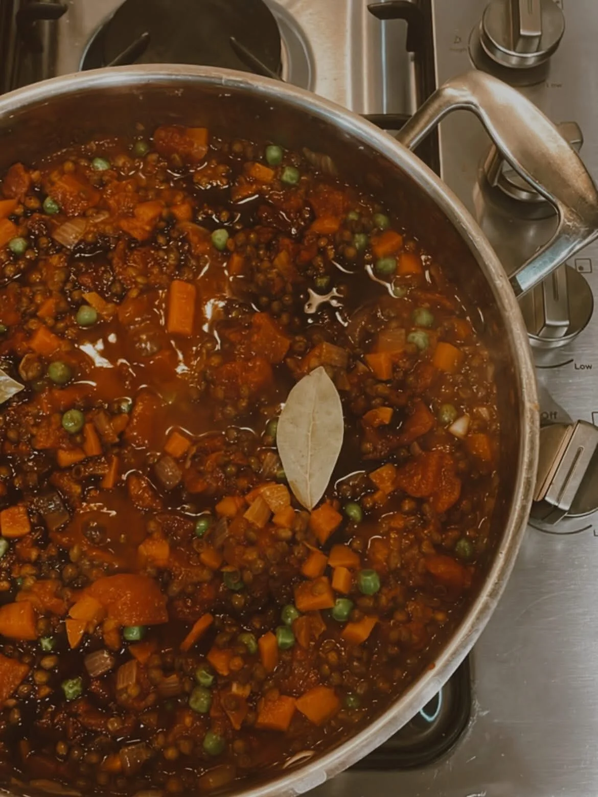 A pot filled with a cooked vegetable and lentil stew simmering on a stove, with a bay leaf floating on top.