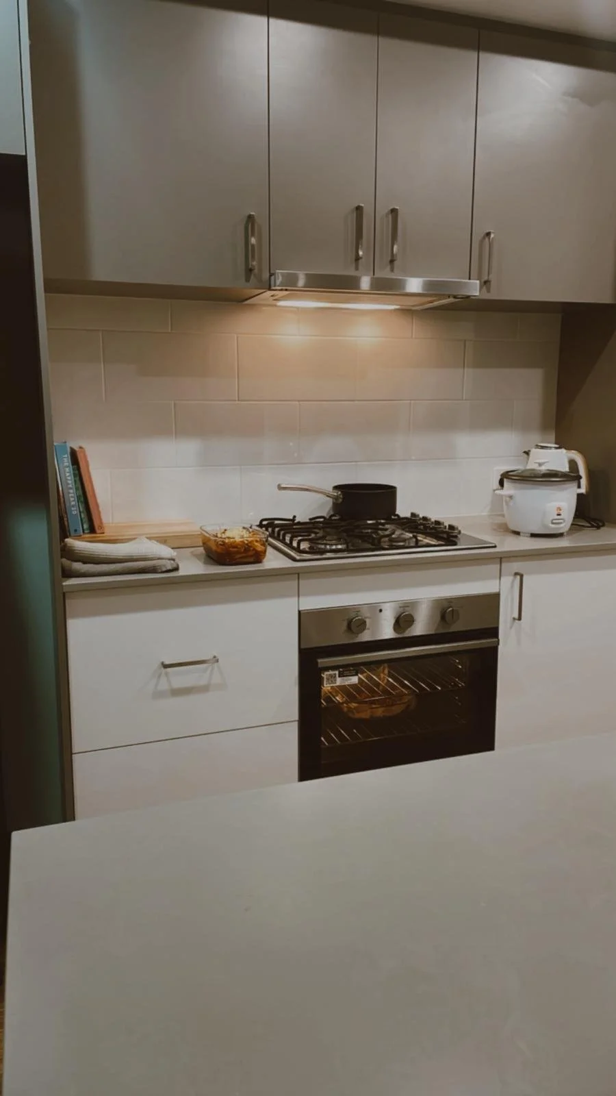 Modern kitchen with beige cabinets, a gas stove with a pot, a toaster, and a glass baking dish on the counter.