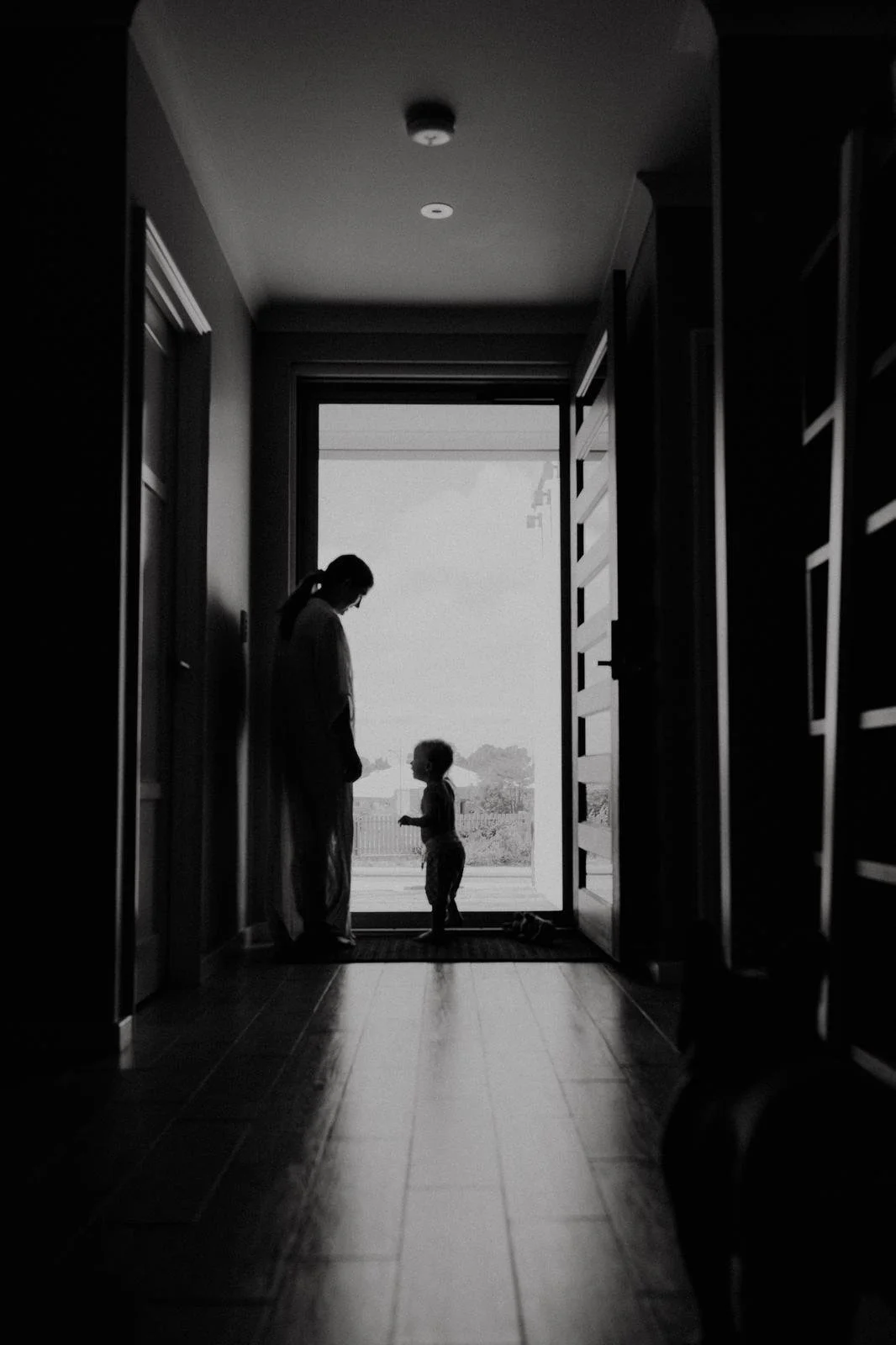 Silhouettes of a woman and a young girl standing in a doorway, with a window showing an outdoor scene in the background.