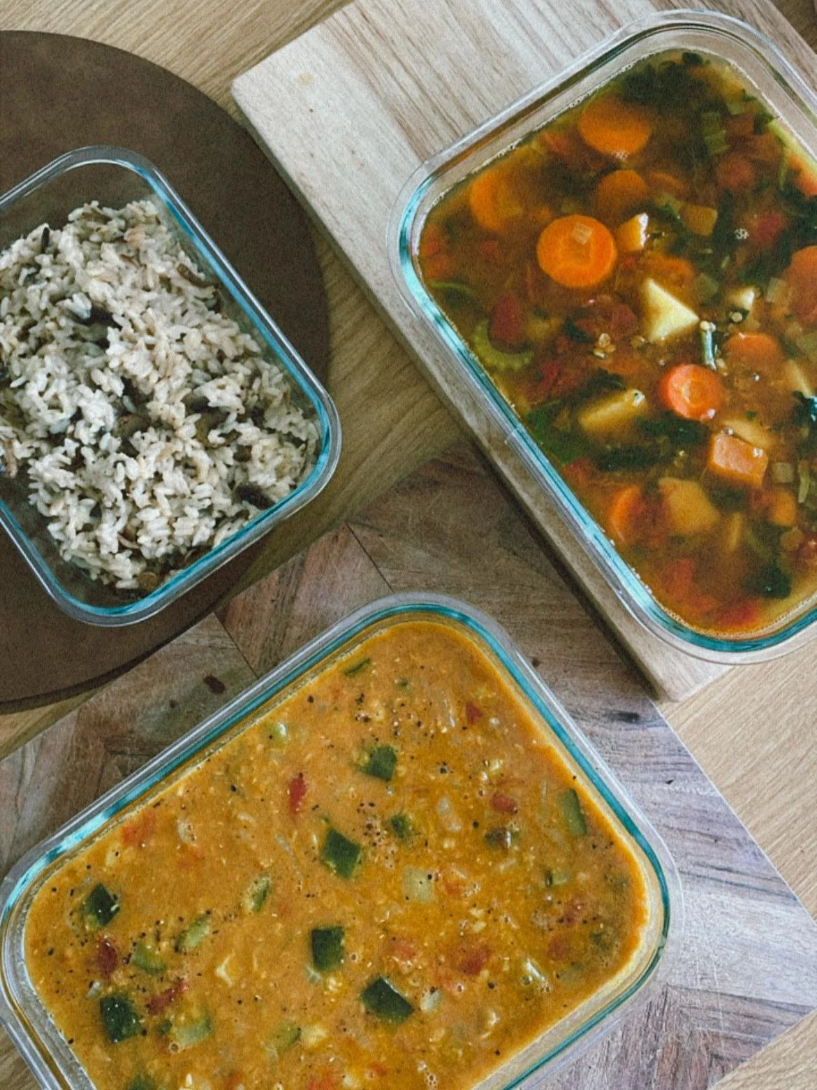 Three glass containers filled with homemade soup and rice on a wooden surface.