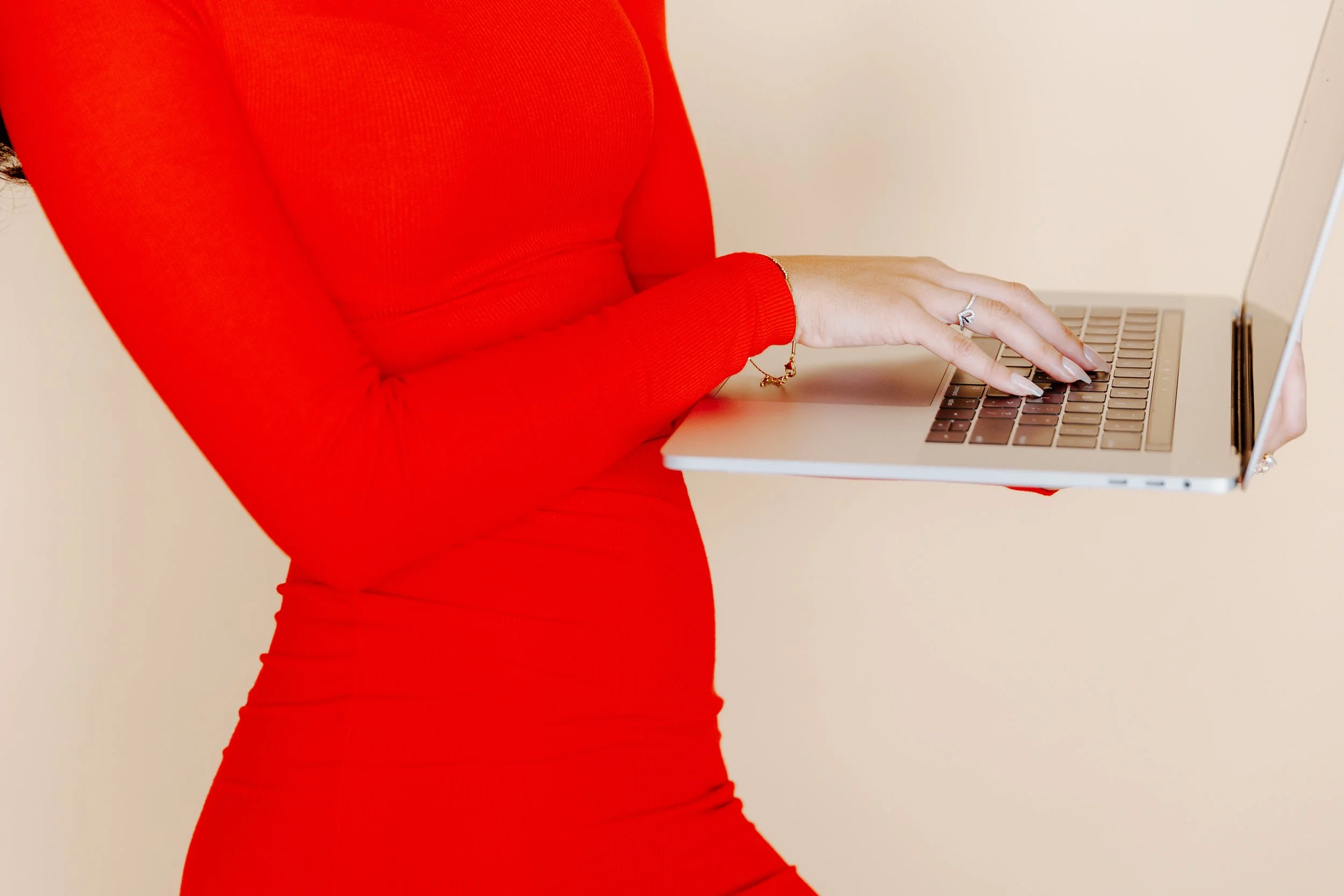 A person wearing a long-sleeved red dress using a silver laptop