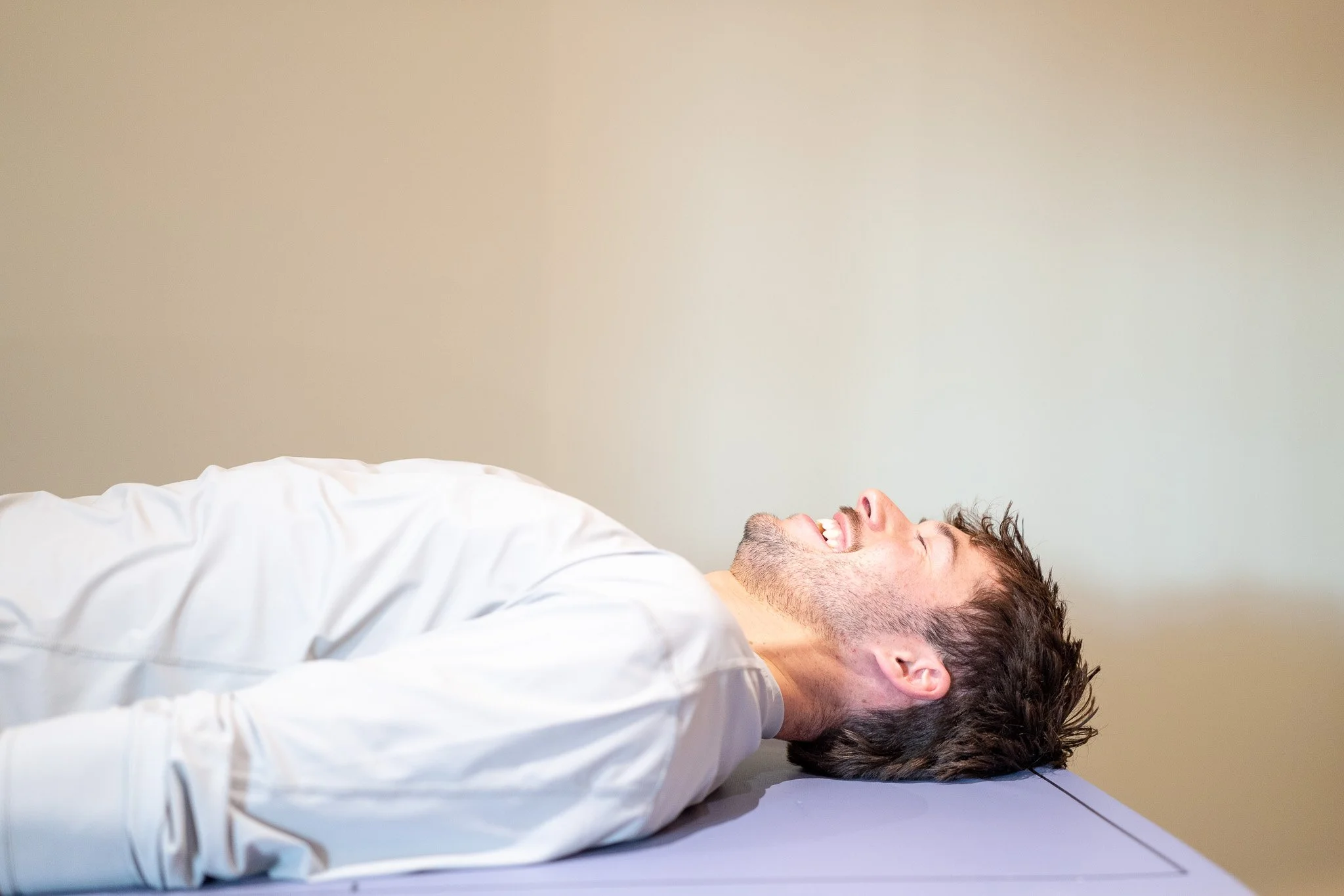 A man lying on his back on a DEXA scanner, smiling and looking relaxed.