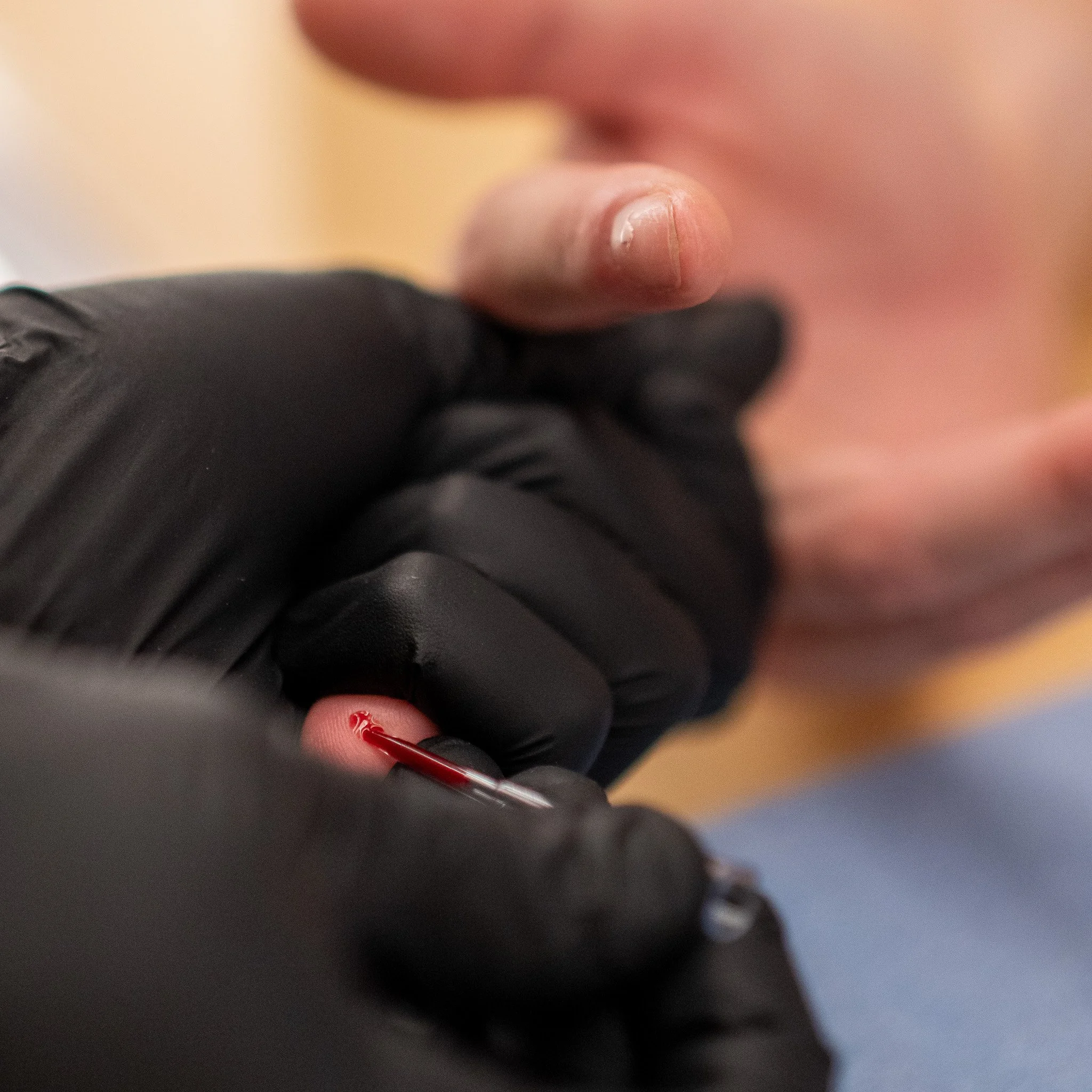 Close-up of a person's finger and a healthcare professional's gloved hand using a thin lancet to perform a blood test.