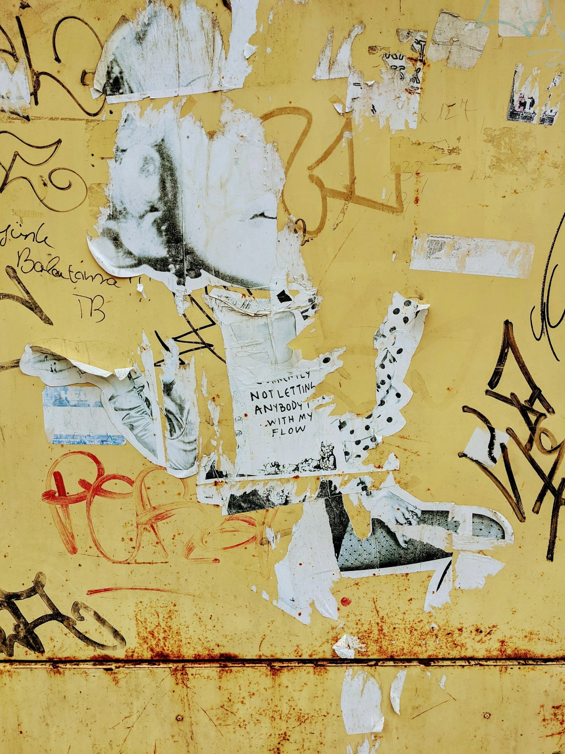 A yellow surface covered with various torn posters, graffiti, and handwritten notes, including a partially visible black and white image of a person's face and some text that reads 'NOT LETTING ANYBODY WITH MY FLOW'.