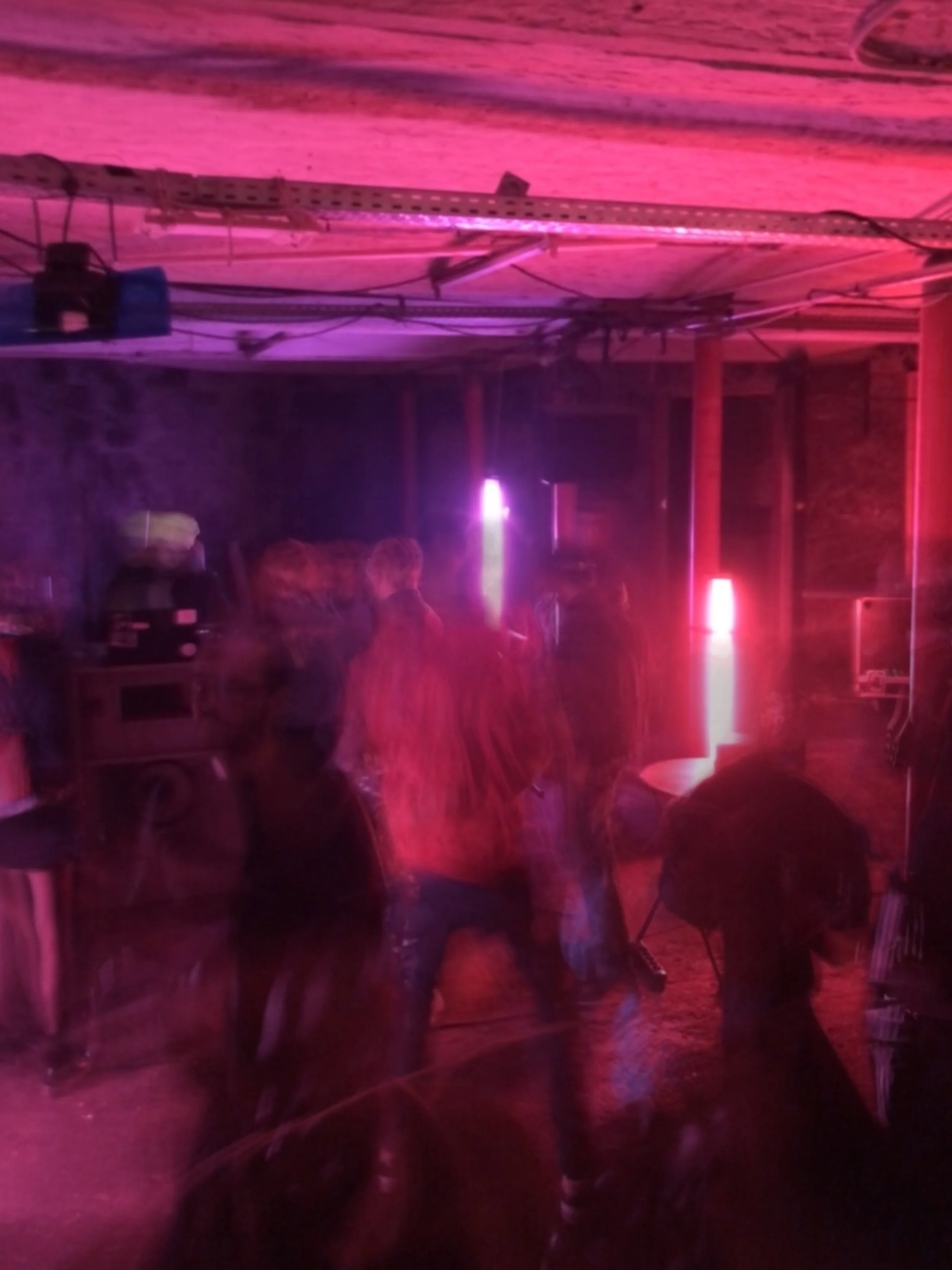 People dancing in a dimly lit room with pink and purple neon lights, blurred movements, and a casual atmosphere.