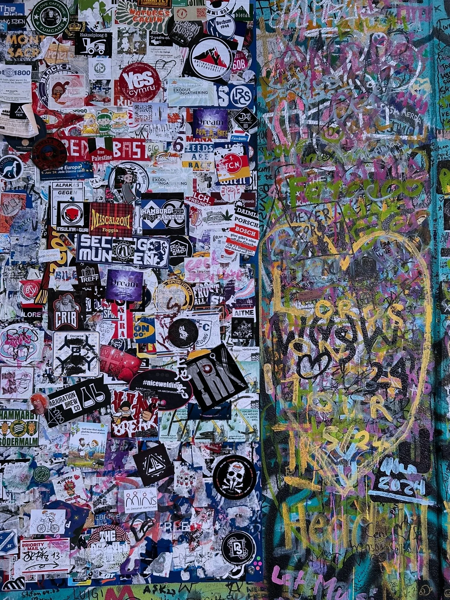 A collage of various stickers, graffiti, and street art on a wall, with colorful layered tags and scribbles on the right side.