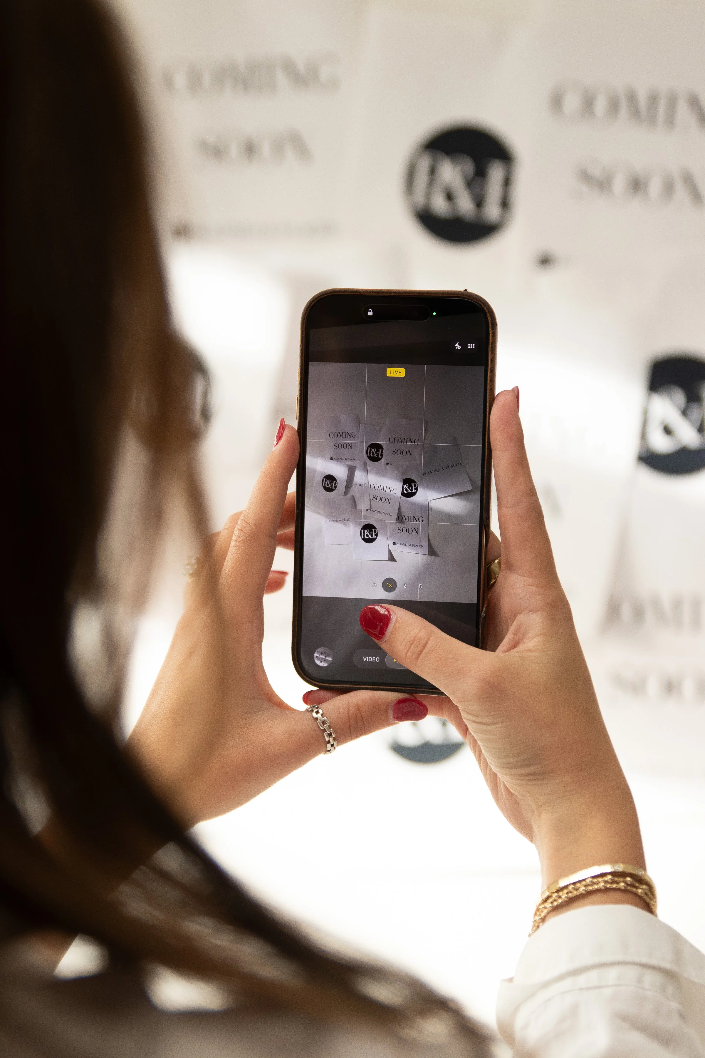 Person taking a photo of a display with notes that say "Coming Soon" and "P&L" on their smartphone at an event or store.