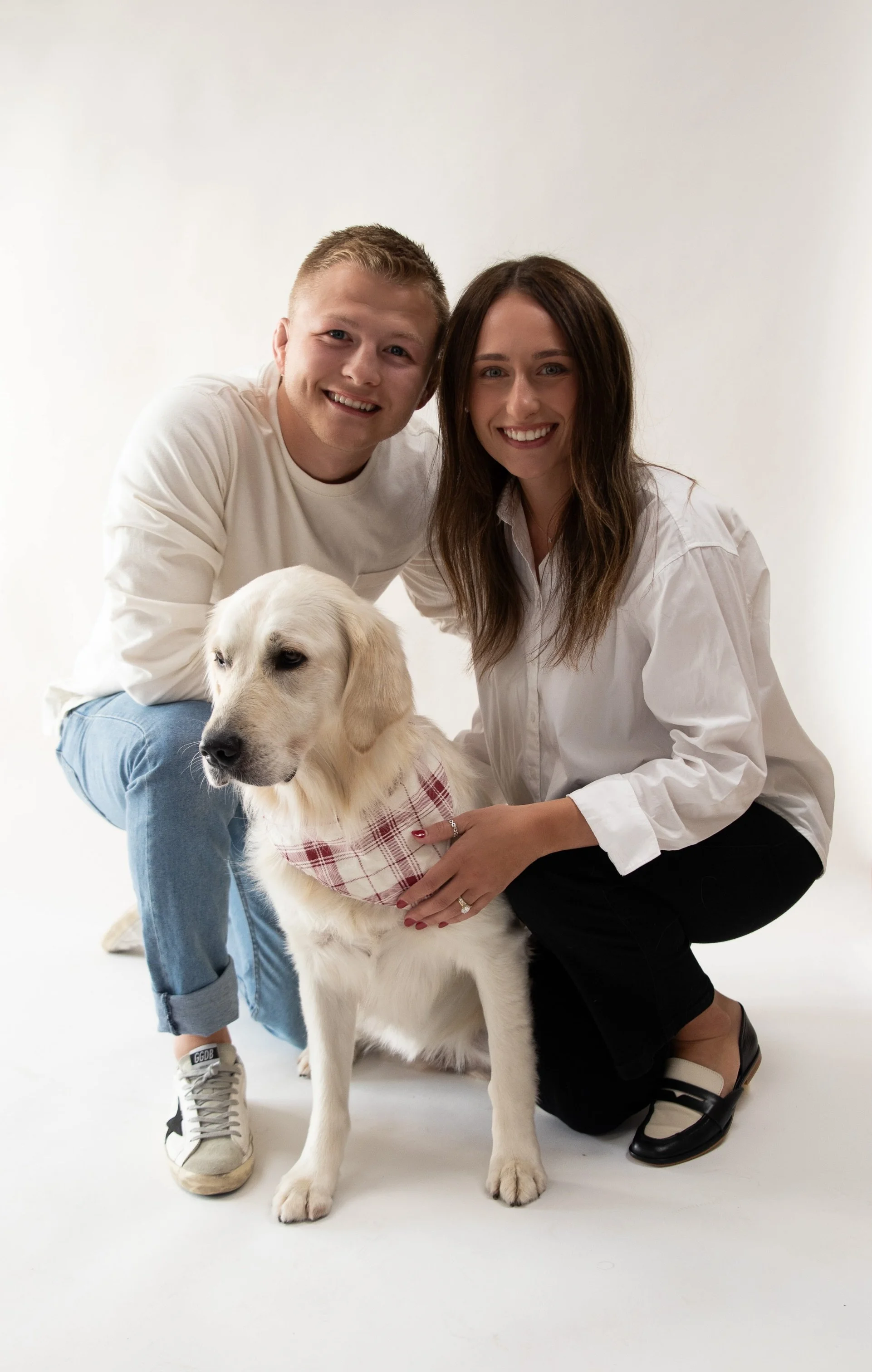 A happy couple with a Labrador retriever dog in a studio with a plain white background.