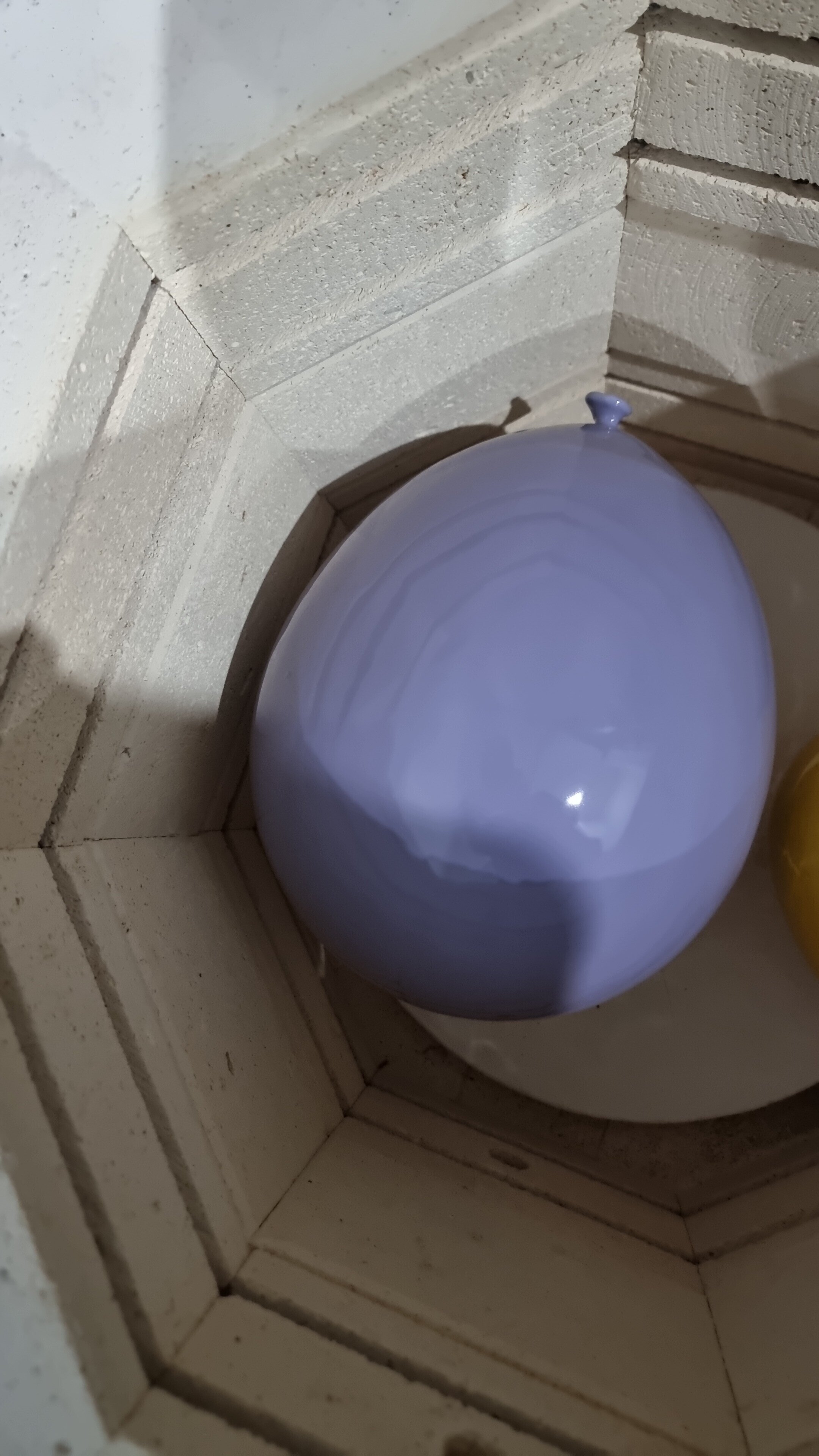 A round, purple and blue glass paperweight placed inside a glass display case with white brick walls.