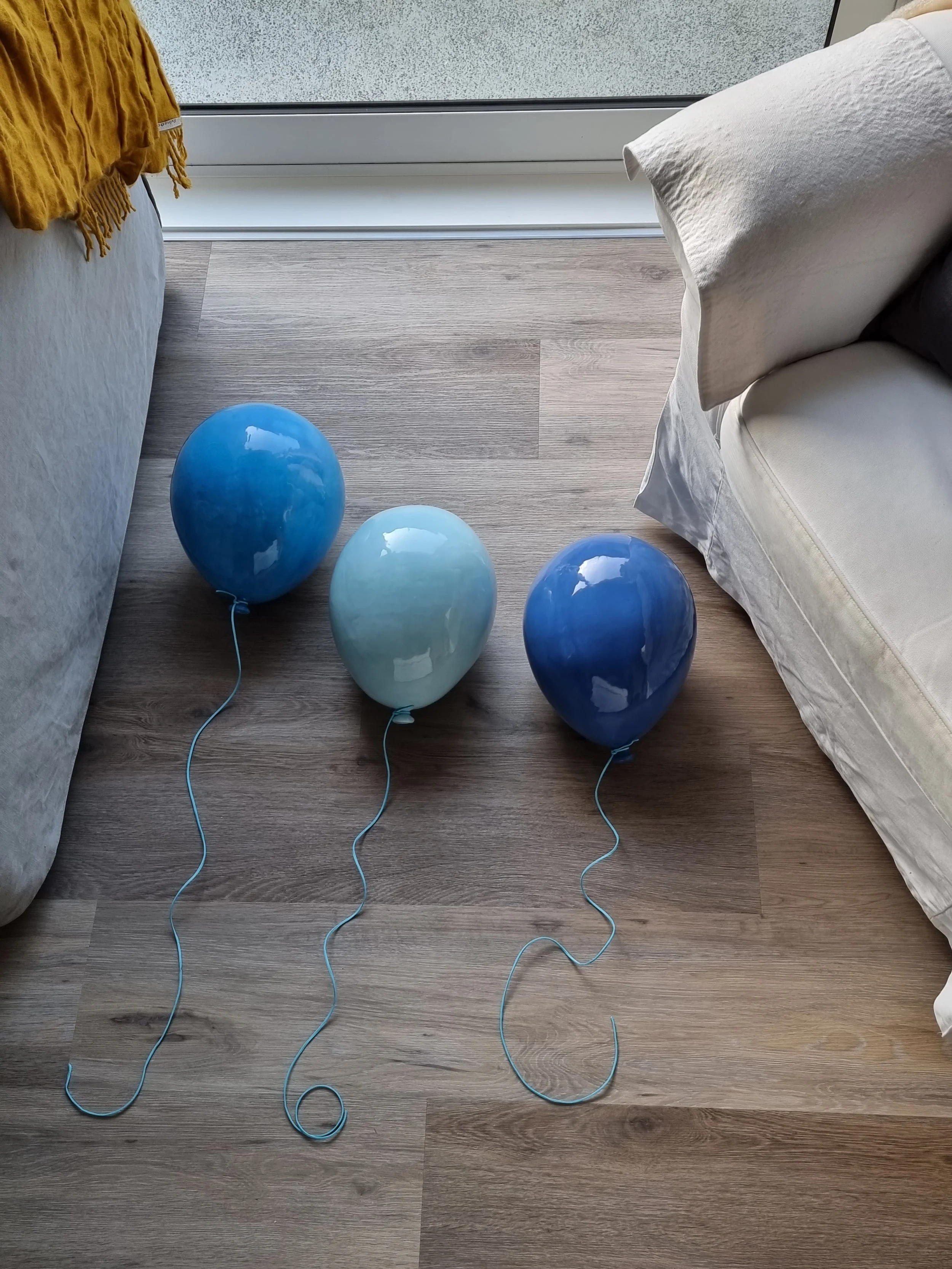 Three helium balloons on the floor between two couches, with a window in the background.