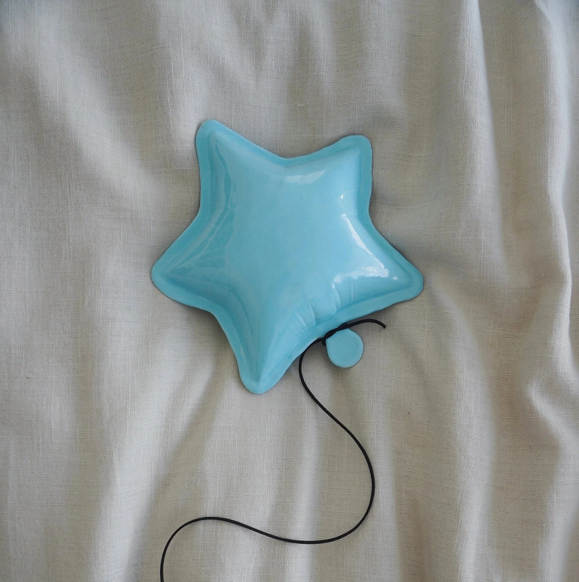 A blue star-shaped night light with a black power cord on a white fabric surface.