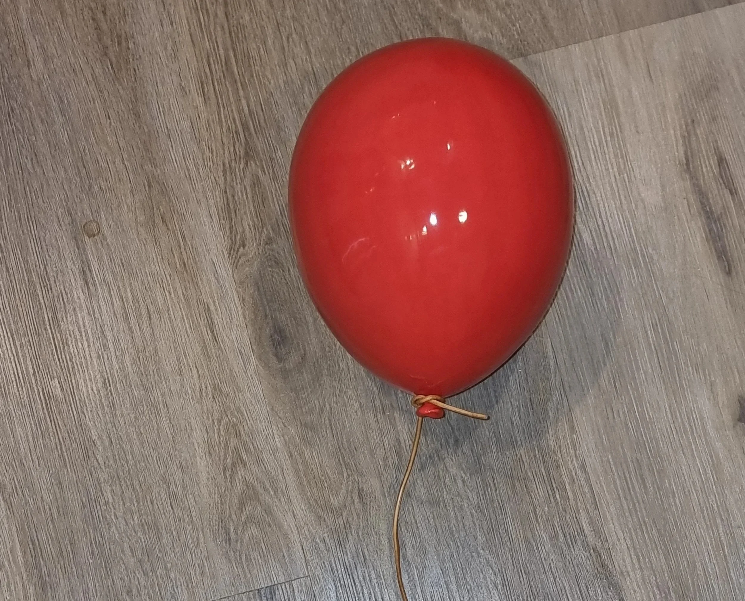 A red helium balloon with a string tied to its knot, resting on a wooden floor.