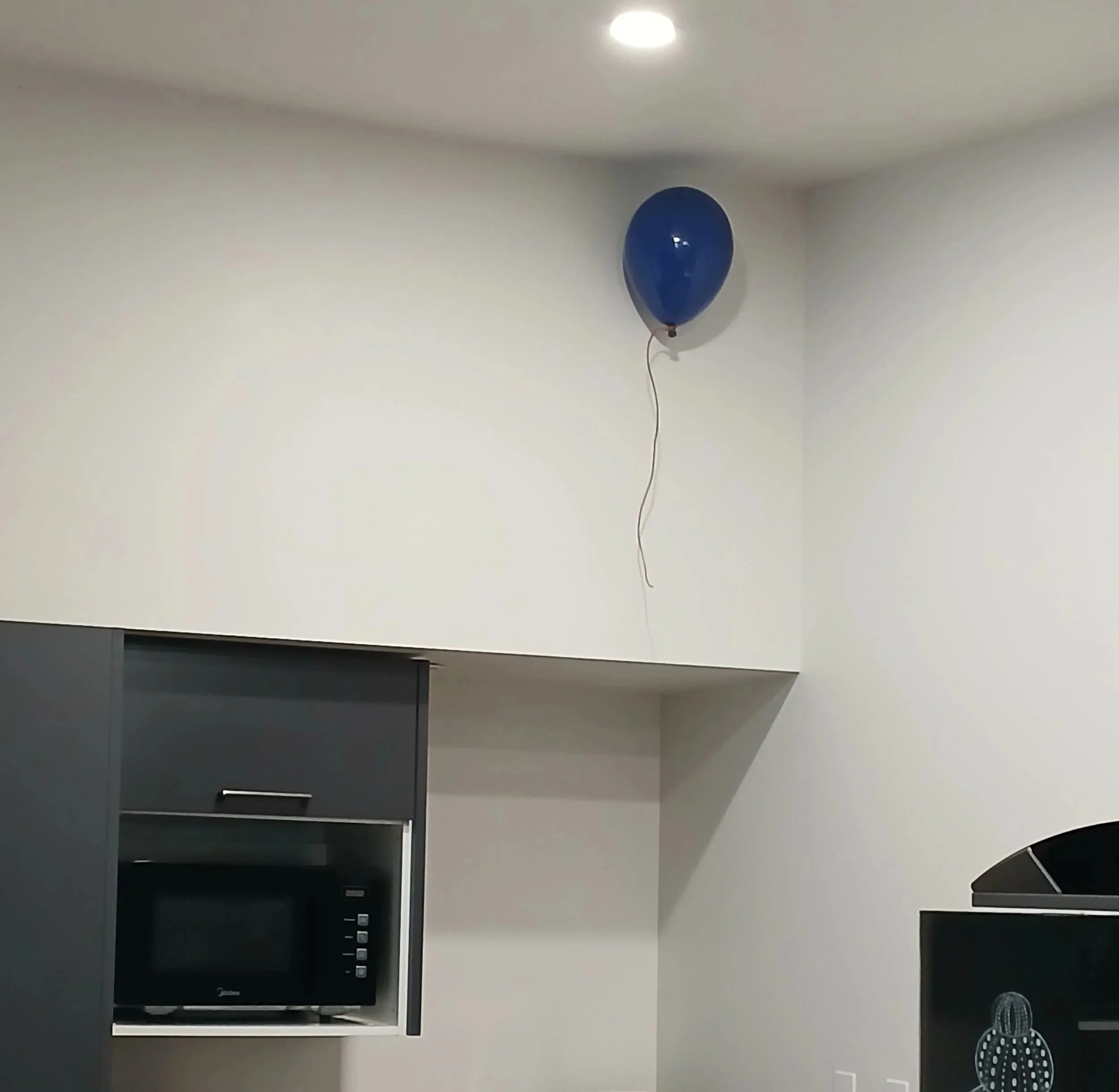 A blue balloon floating near the ceiling in an interior kitchen space with white walls and modern appliances.