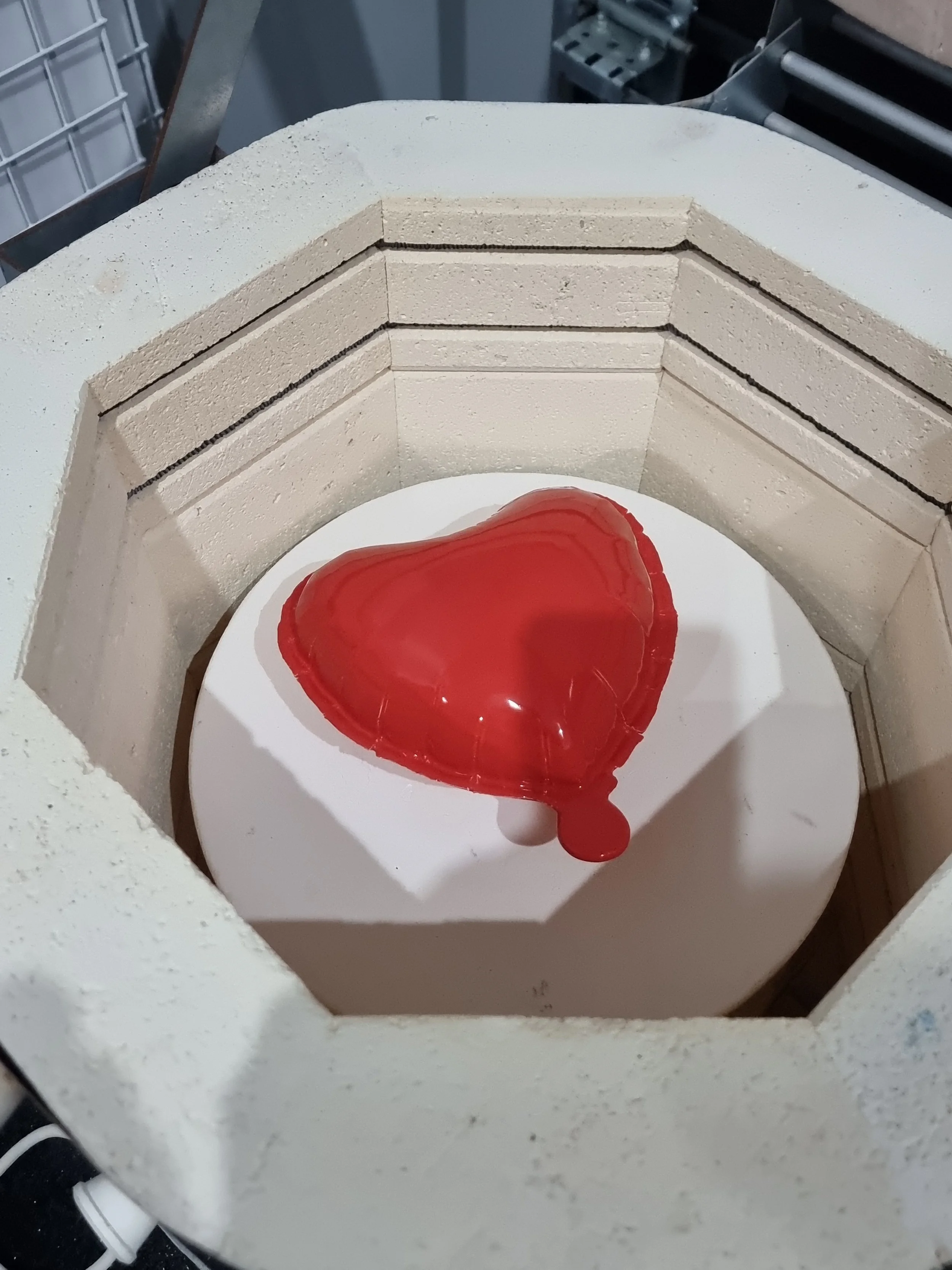A heart-shaped red balloon breaking inside a kiln with a brick lining.