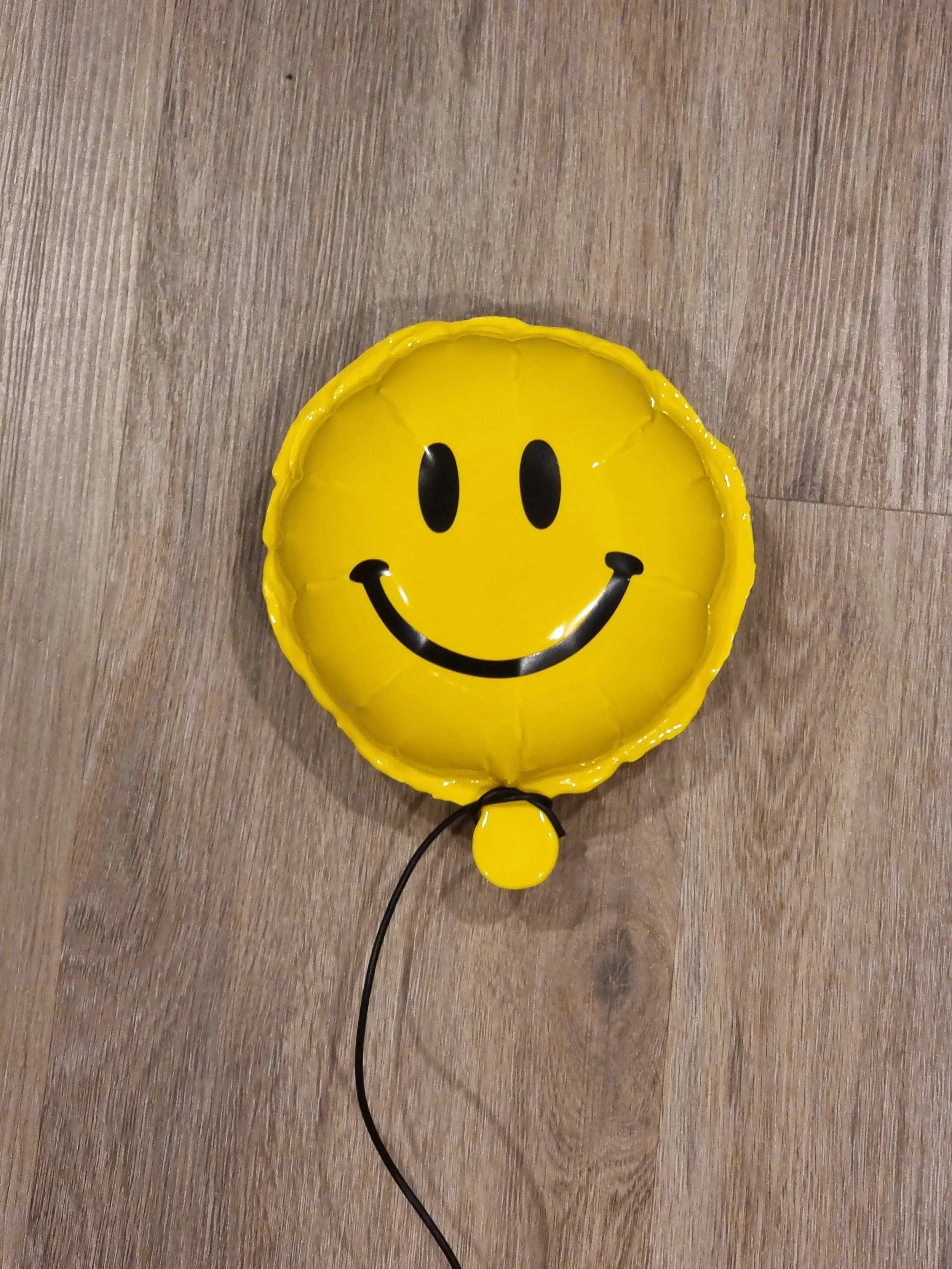 Yellow smiley face balloon with black eyes and a smile, on a wooden floor.