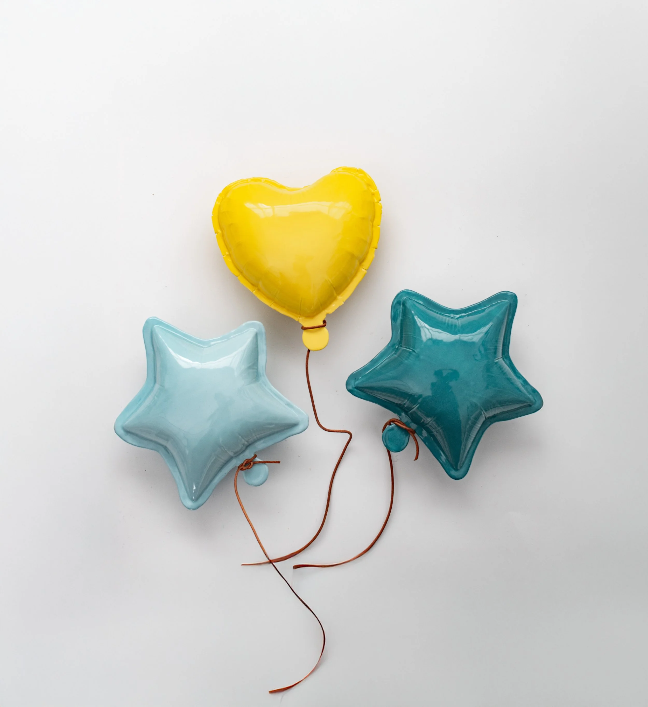 Three balloons shaped like stars and a heart with strings attached, on a white background.